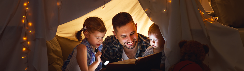 Man and two kids reading book under fort
